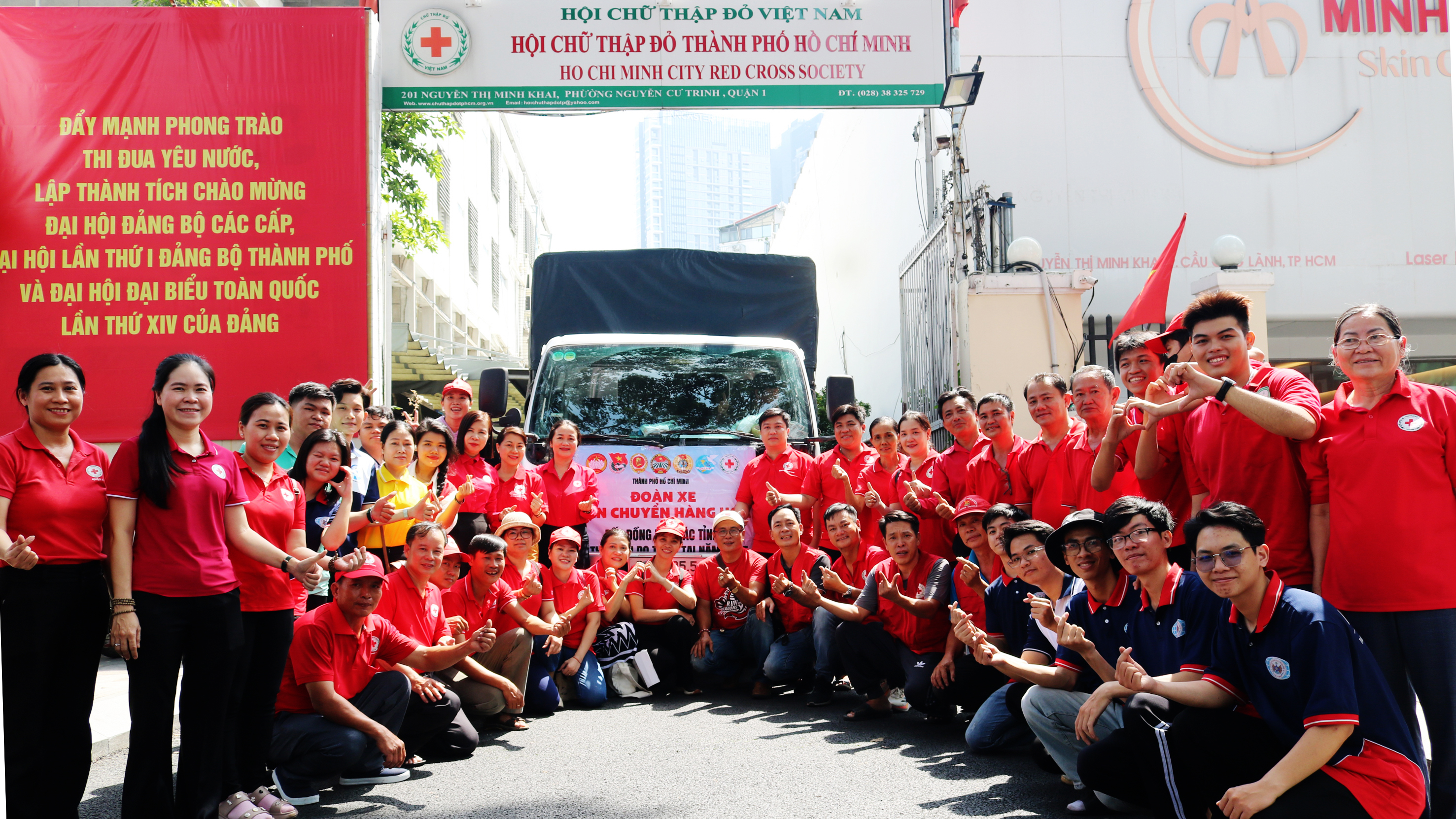 Đông đảo tình nguyện viên Chữ thập đỏ áo đỏ chụp ảnh cùng đoàn xe vận chuyển hàng trước trụ sở Hội Chữ thập đỏ Thành phố Hồ Chí Minh