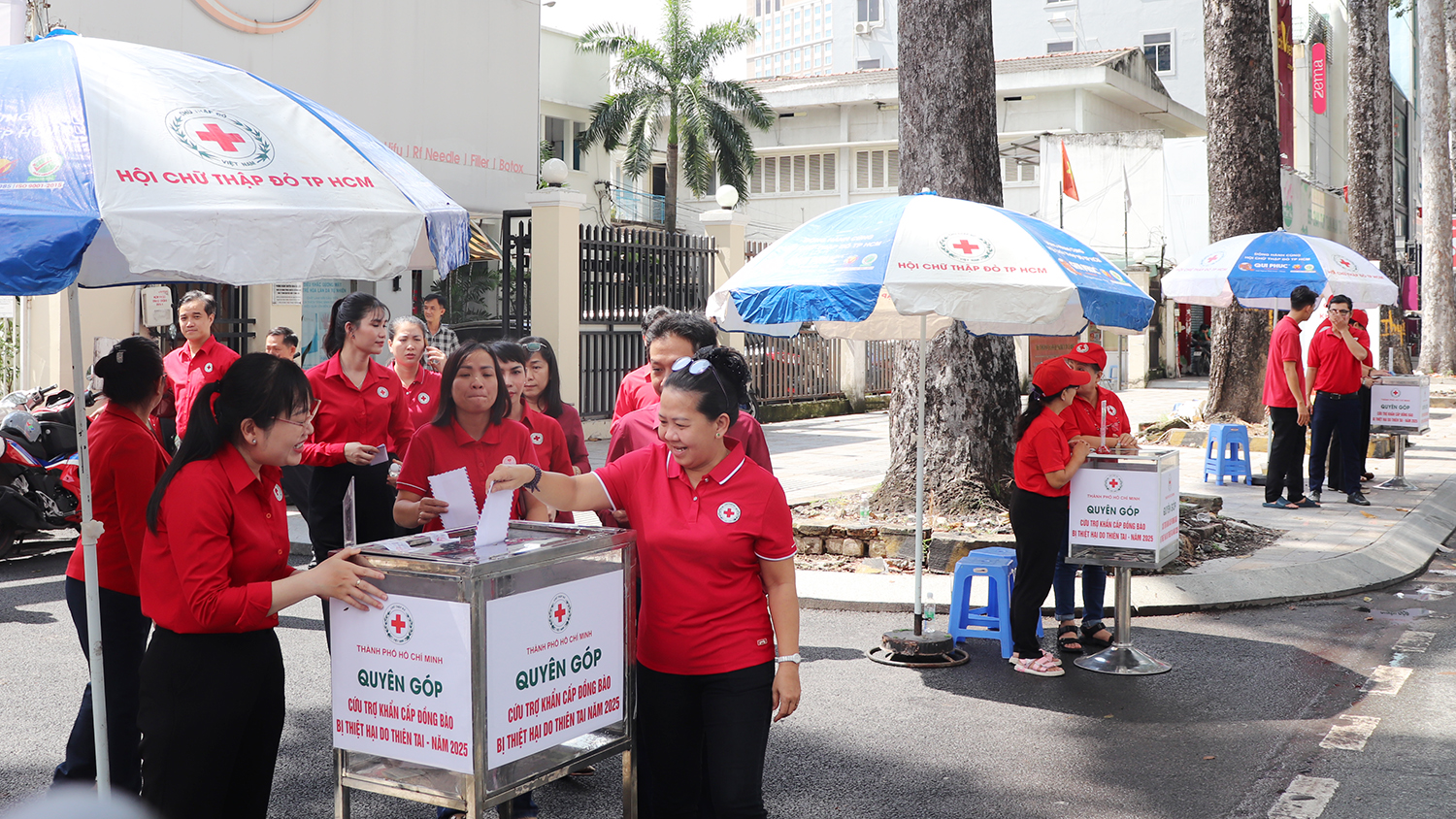 Cán bộ Hội Chữ thập đỏ áo đỏ bỏ tiền ủng hộ vào thùng quyên góp đặt trước trụ sở Hội Chữ thập đỏ Thành phố Hồ Chí Minh